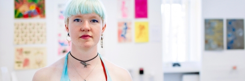 A woman with blue hair standing in front of artwork