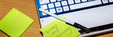 Green sticky note reading "essay due wednesday" on laptop