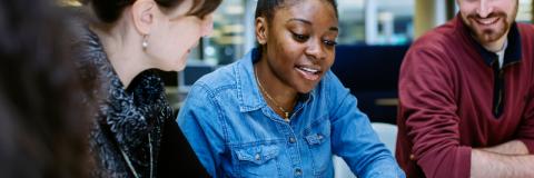 Staff member talking to two students at a table, supporting them with some of their work
