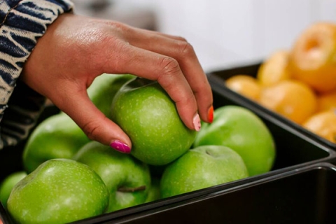 A shopper's hand reaching for some apples in a supermarket