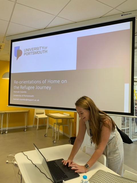 Hanna Coombs setting up her laptop at the front of a lecture theatre. Her presentation is on the screen behind her.