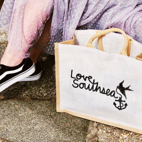 A Love Southsea hessian bag next to someone wearing a pink skirt and Vans