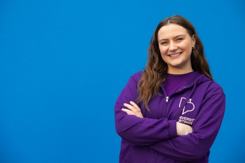 University ambassador standing and smiling against blue background