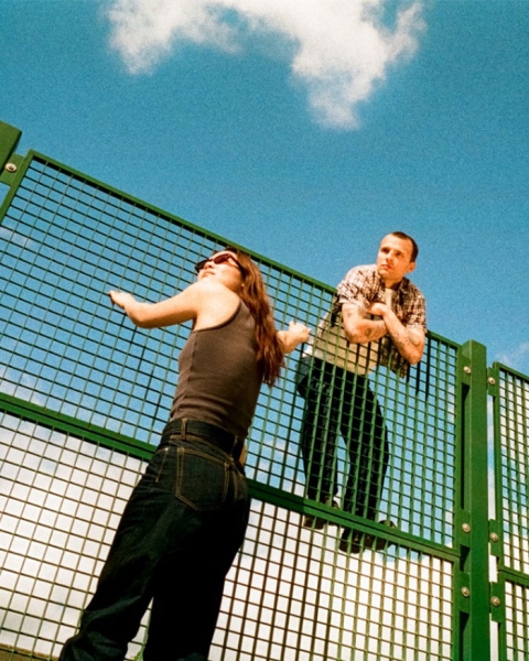 Two students on a fence with a blue sky backdrop