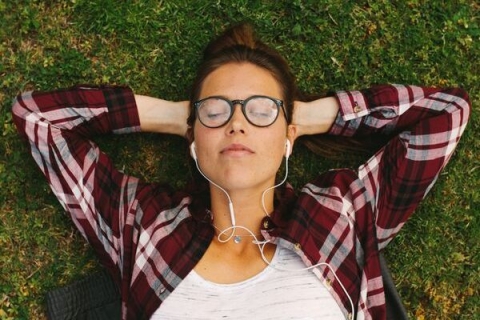 female student lying on the grass wearing headphones