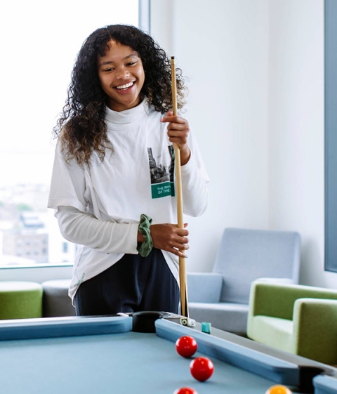A student smiling while playing pool