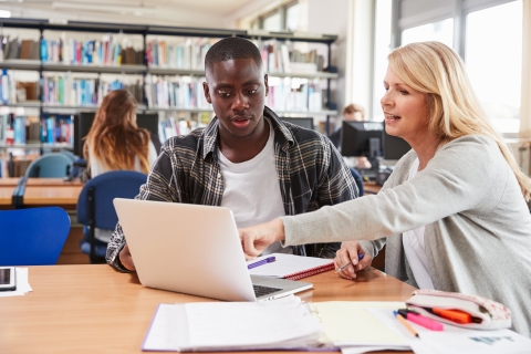 A teacher with a student, both looking at a laptop