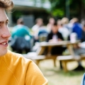 Students chatting at a picnic bench in the park, one wearing a yellow jumper and the other a denim jacket