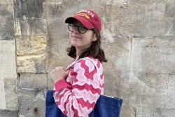 Placement student Lucille pictured against a grey wall holding a blue bag