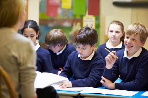 School children in a classroom, sitting at a desk with workbooks