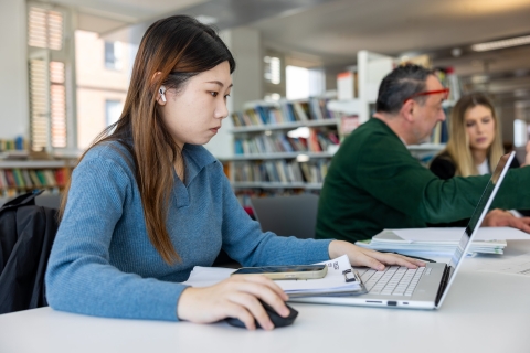 Female student with long hair in the library on a computer