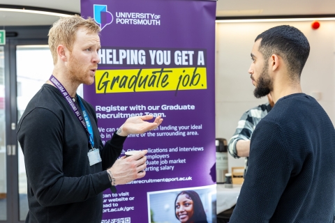 Two men speaking in front of a graduate jobs banner