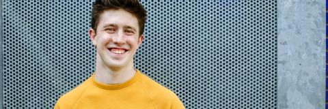 Smiling male student stood outside in yellow jumper